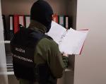 Funkcjonariusz KAS, w kominiarce zasłaniającej twarz, przegląda dokument w segregatorze 