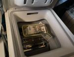 pralka otwierana od góry. widoczny bęben pralki na którym leży plastikowy koszyk z banknotami