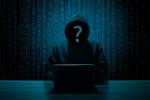Na grafice osoba będąca hakerem, siedząca przy stole przed laptopem w bluzie z kapturem. Zamiast twarzy na czarnym tle jest znak zapytania. W tle czarne tło z małymi cyframi.