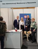 Pracownicy i funkcjonariusze Służby Celno-Skarbowej na stanowisku KAS stoją z psem służbowym. Z tyłu baner z logo KAS
