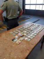 Banknoty ułożone w kupki leżą na stole. Obok stoi funkcjonariusz SCS.