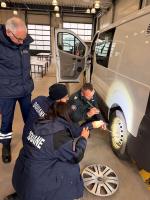 Funkcjonariusz SCS i przedstawiciele Administracji Celnej Francji przy samochodzie odkręcają śruby.