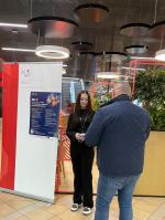 Ekspertka stoi przy stanowisku. Przed nią odwiedzający galerię.