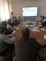 Ekspertka stoi przed uczestnikami spotkania. Na ekranie wyświetlana jest prezentacja.