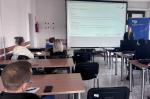 Uczestnicy szkolenia siedzą w sali. Na ekranie wyświetlana jest prezentacja.