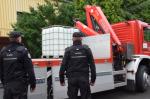 funkcjonariusze Służby Celno- Skarbowej nadzorują załadunek pojemników z alkoholem, w tle samochód Straży Pożarnej