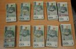 pieniądze wykryte podczas kontroli. 100- złotowe banknoty leżą na stole w dziesięciu plikach. Każdy plik banknotów  owinięty jest cienką gumką.