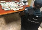 funkcjonariusz Krajowej Administracji Skarbowej podczas kontroli dewizowej, na stole znajdują się pliki z banknotami i liczarka banknotów